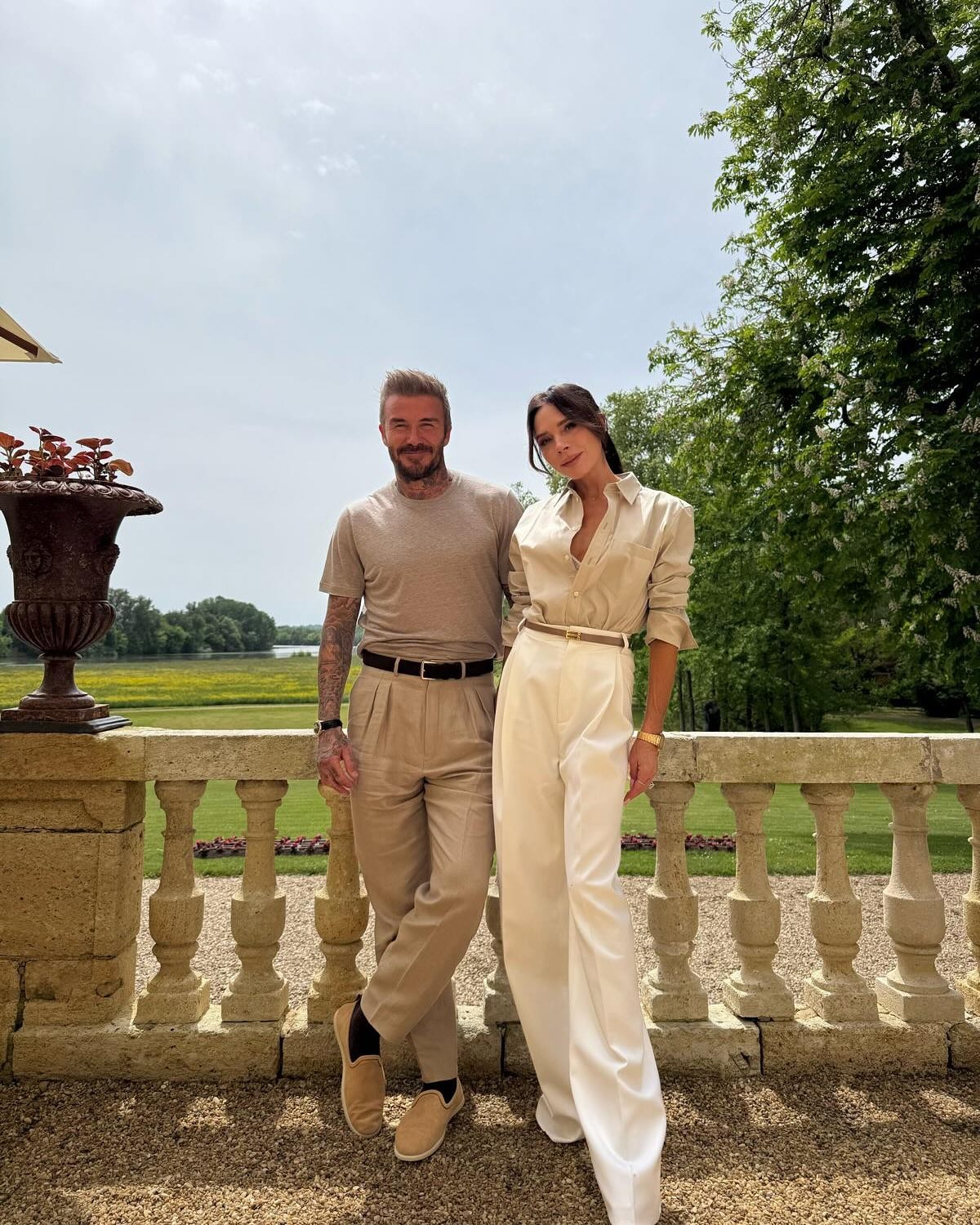 David and Victoria Beckham in neutral-toned outfits, standing on a balcony with a scenic landscape behind them.