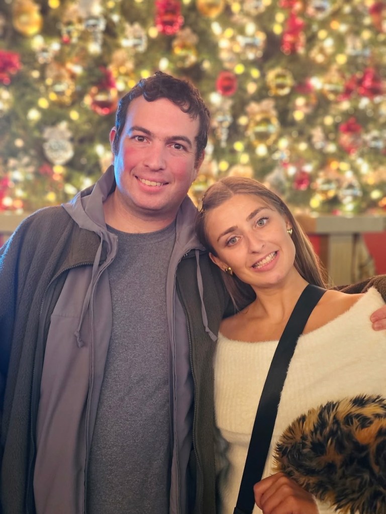 Abbey Romeo and David Isaacman smiling in front of a Christmas tree.