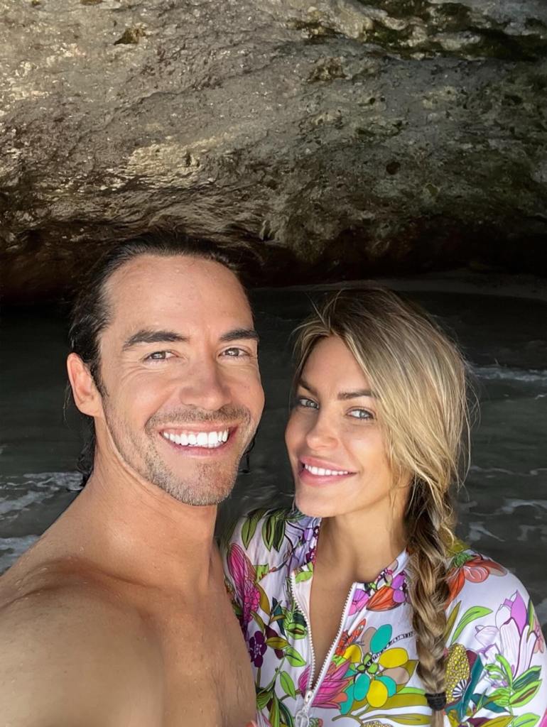 Crystal Harris and James Ward smiling at the camera in a grotto with water.