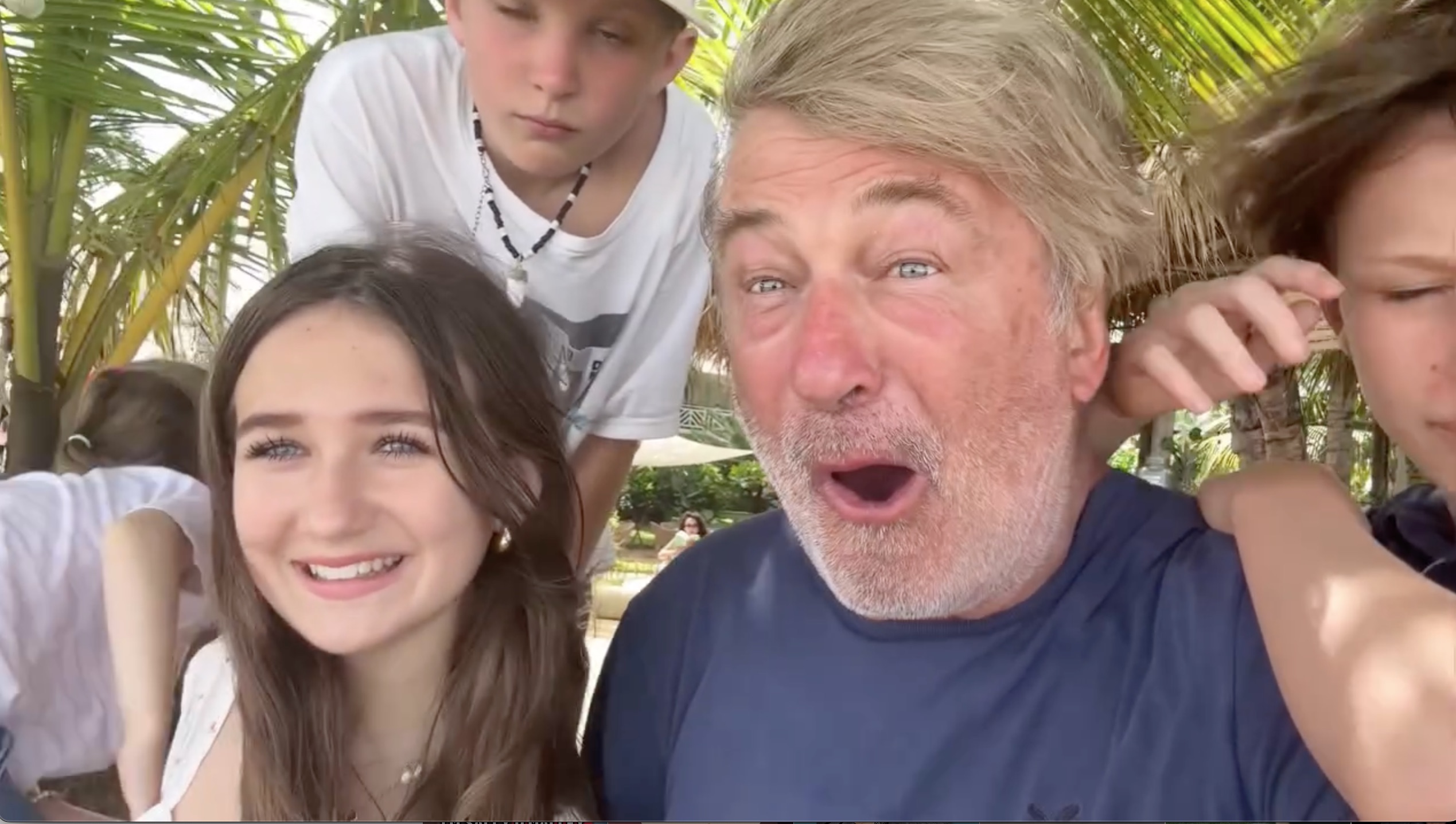 Alec Baldwin with three of his children, one smiling at the camera, and one with their hand on his shoulder.