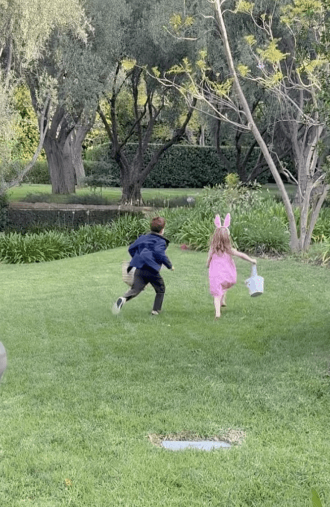 Two children running across a grassy lawn with Easter baskets.