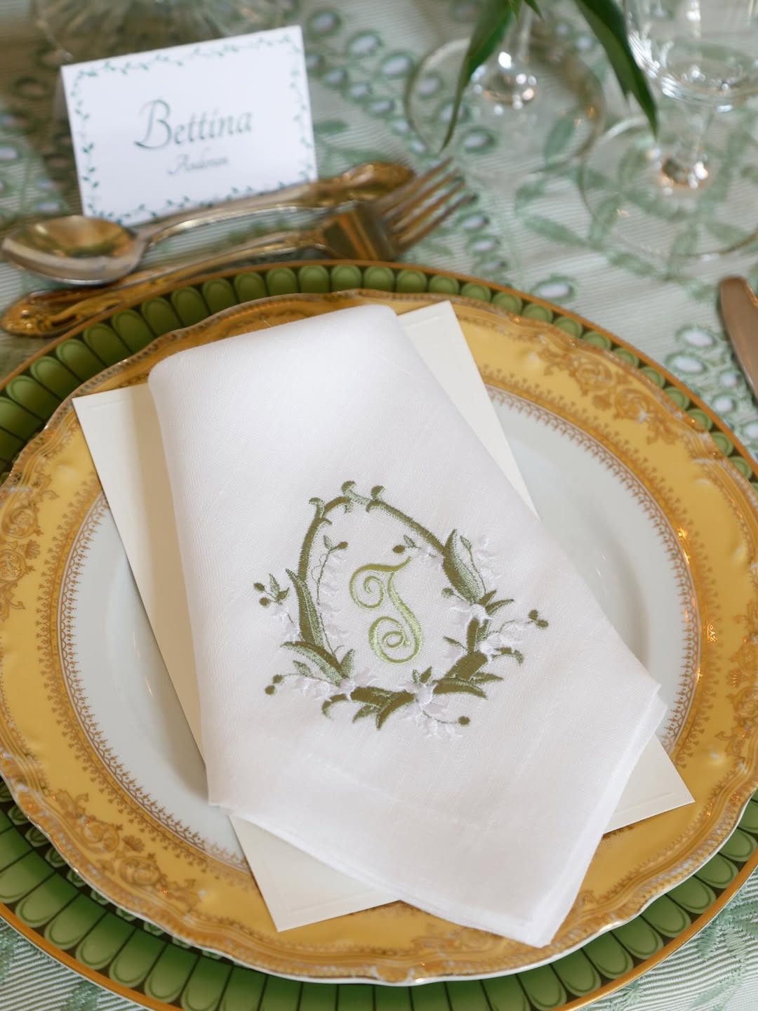 A formal place setting with a white napkin embroidered with the letter