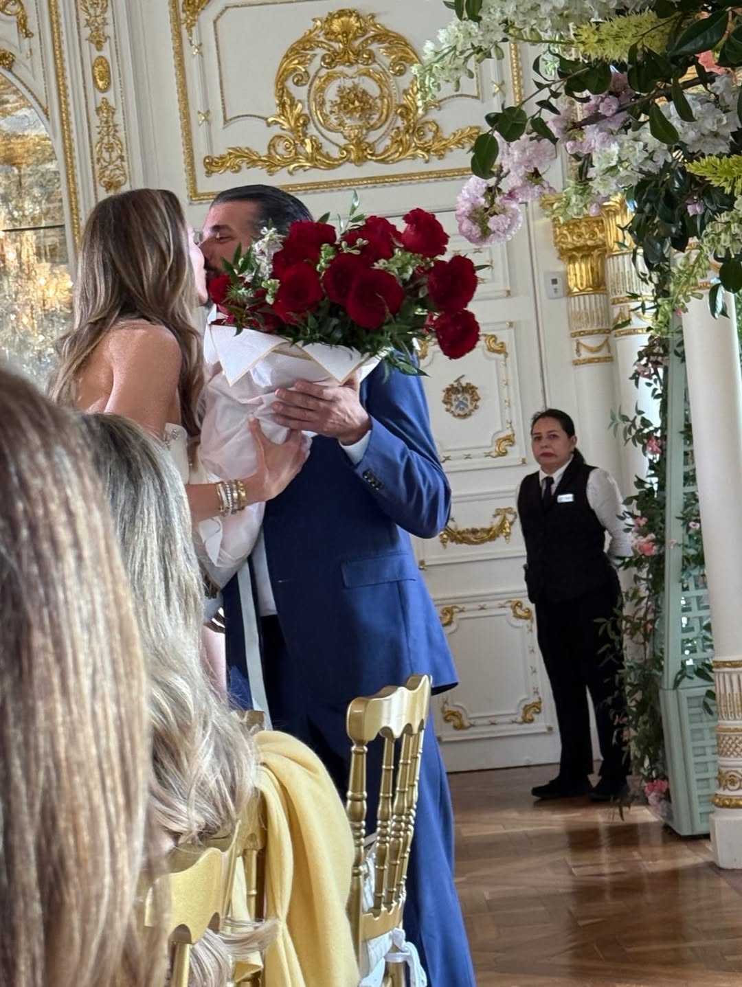 Donald Trump Jr. in a blue suit kisses Bettina Anderson while holding a bouquet of red roses.
