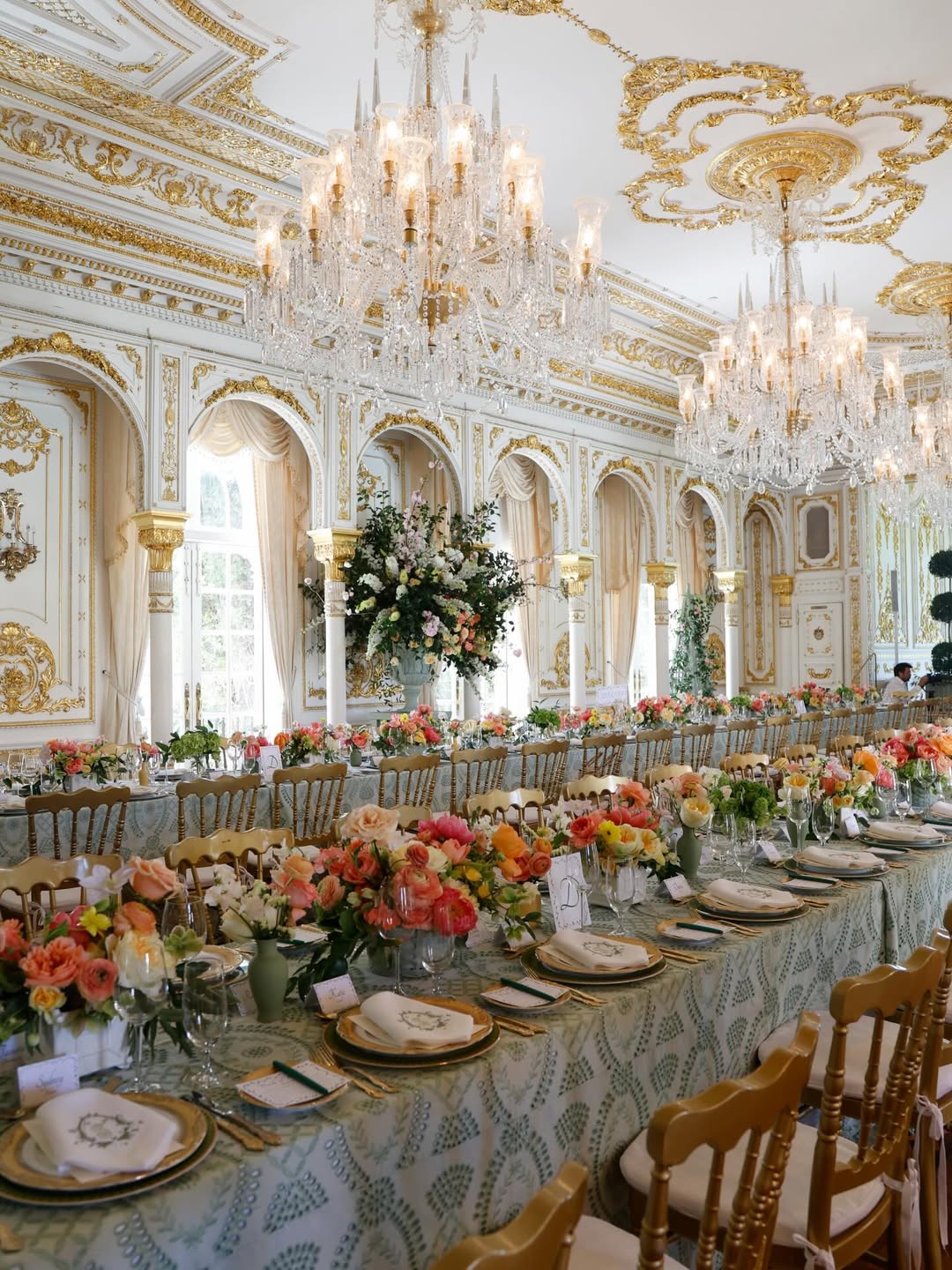 A lavish banquet hall decorated for a bridal shower with multiple chandeliers and long tables adorned with colorful floral arrangements.