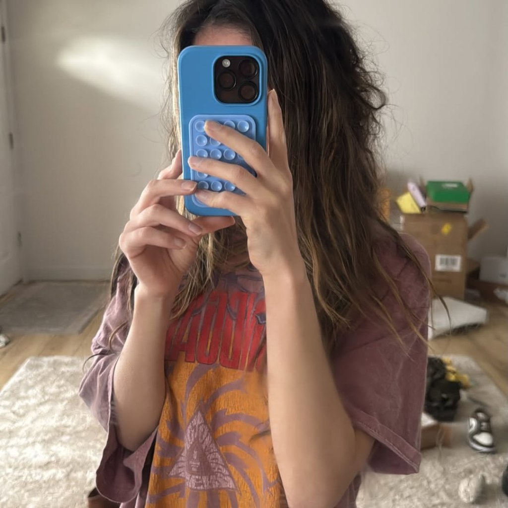 A woman in a graphic t-shirt holds a blue phone with a pop-it style case, obscuring her face.