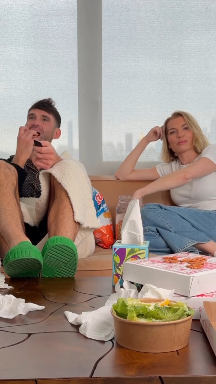 Lindsay Hubbard and Carl Radke sitting on a sofa with food and tissues, as if watching a sad movie.