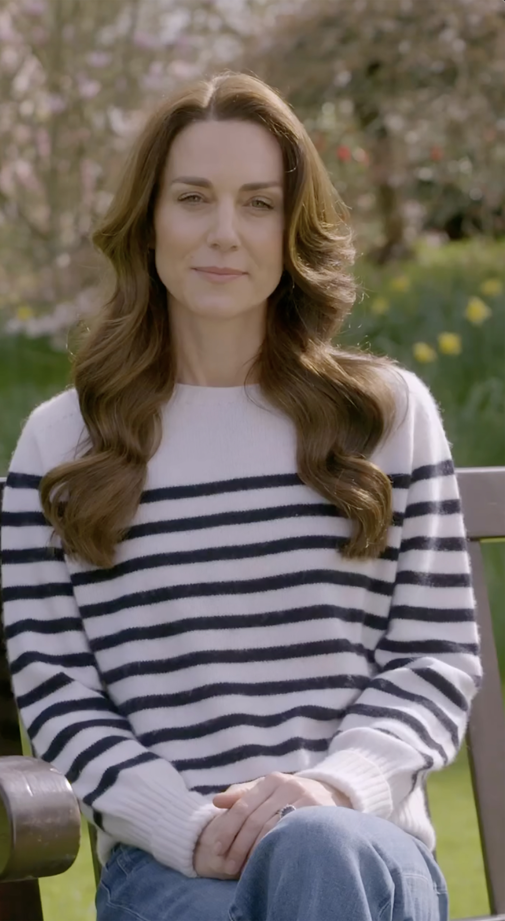 Kate Middleton in a striped sweater sitting on a bench outdoors.