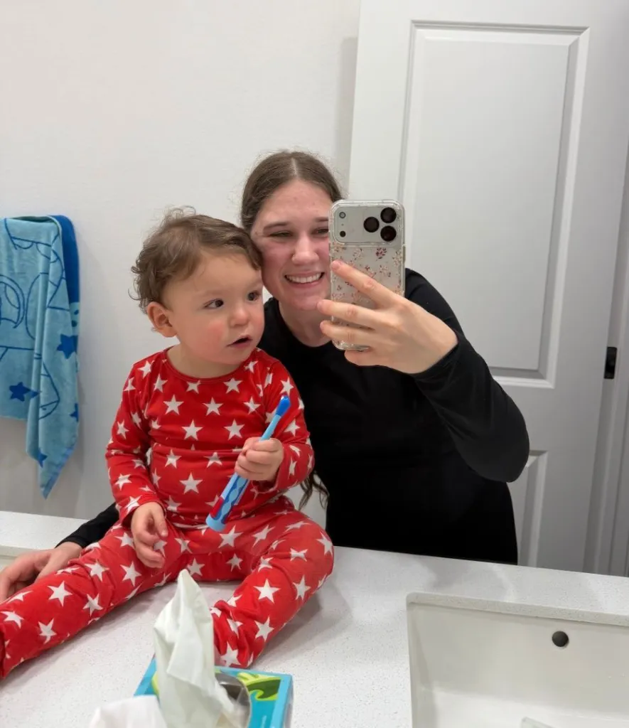 A woman holding a phone in the mirror, taking a selfie with a baby.