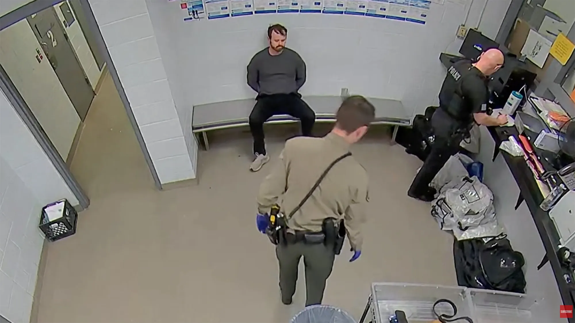Joseph Duggar during his arrest, seated with his hands cuffed behind him, with two officers in the room.