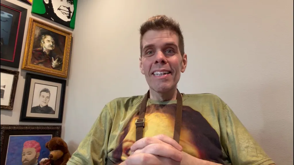 Perez Hilton speaking to the camera, wearing a T-shirt with an image of Jesus and a brown apron, with various framed art and a teddy bear behind him.