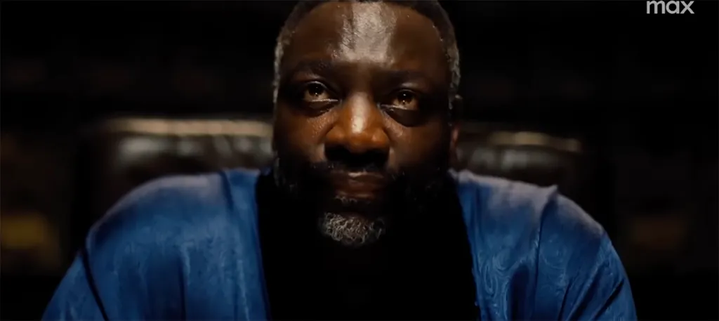 Adewale Akinnuoye-Agbaje in a blue robe, looking intensely forward.