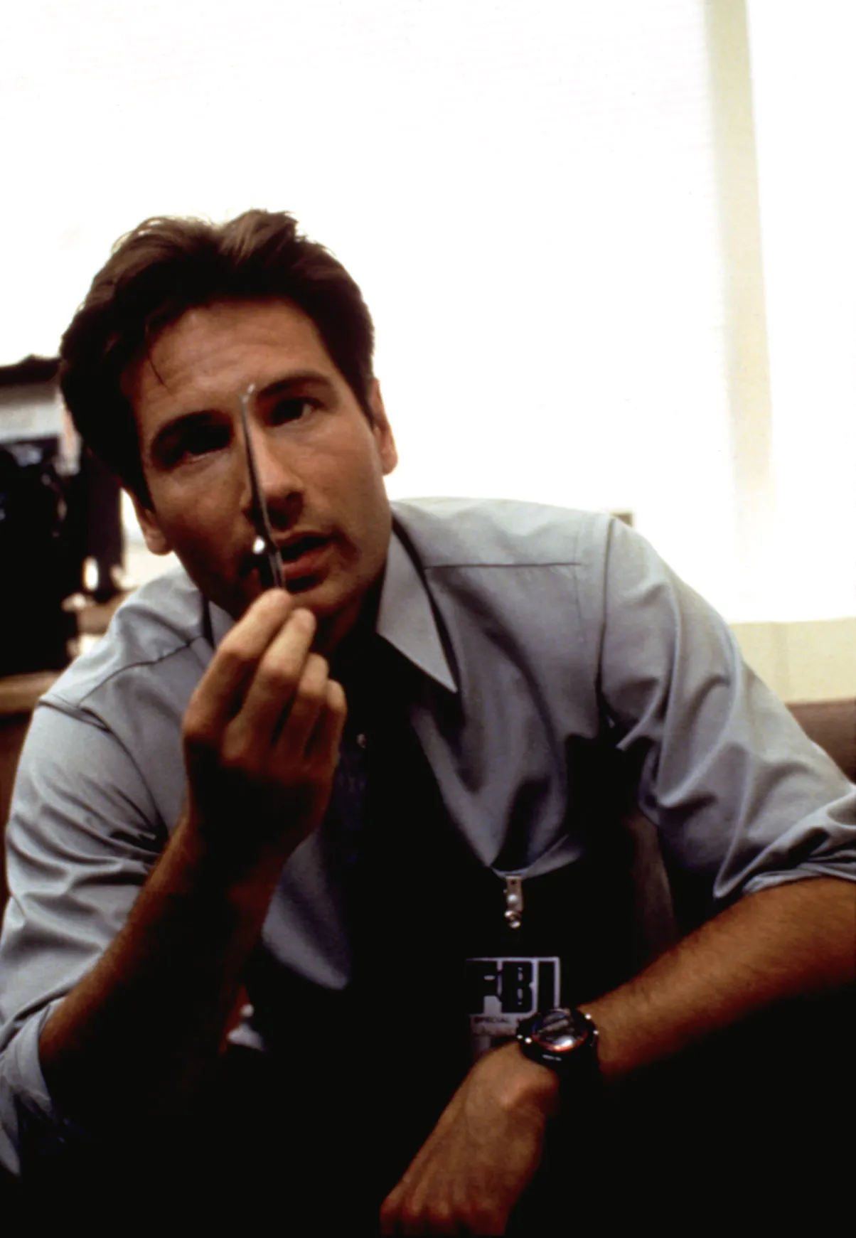 David Duchovny as Fox Mulder in The X-Files, holding a small object in front of his face.