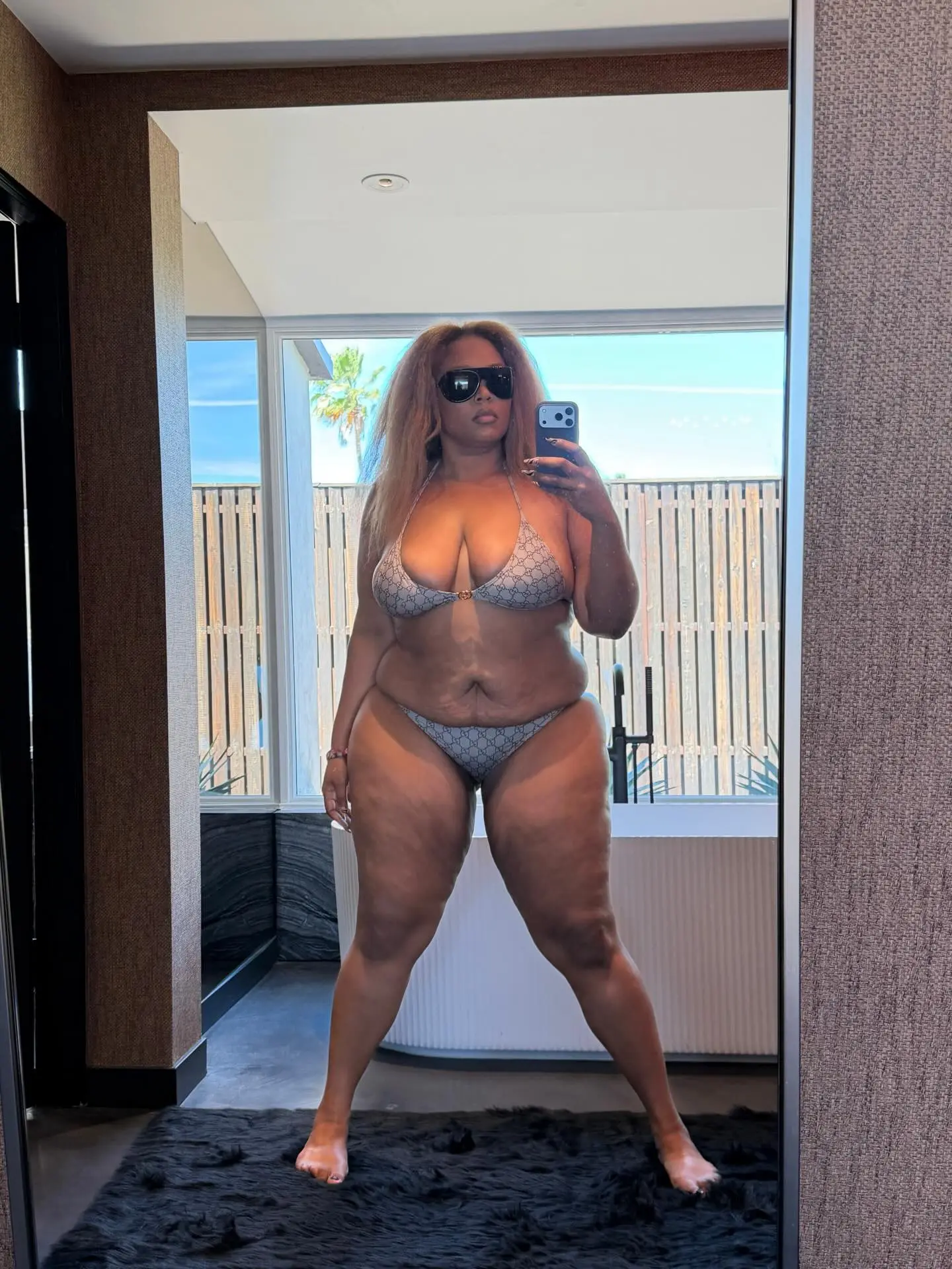 Lizzo in a Gucci bikini and sunglasses, taking a mirror selfie.