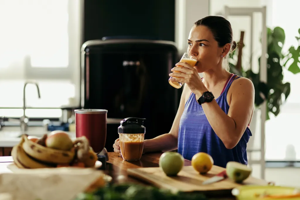 Woman in athletic wear drinking a fruit smoothie in her kitchen.