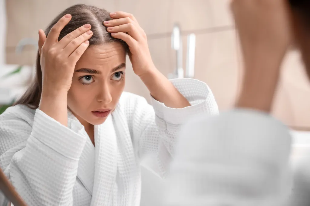 Young woman looking in the mirror, concerned about hair loss.