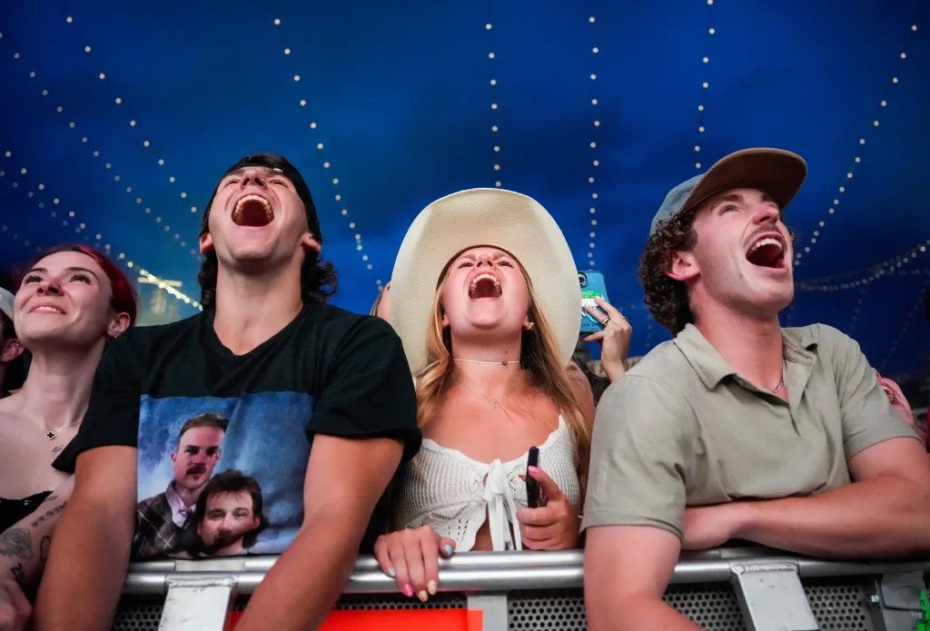 Concert-goers cheering with mouths open, looking up at the stage.