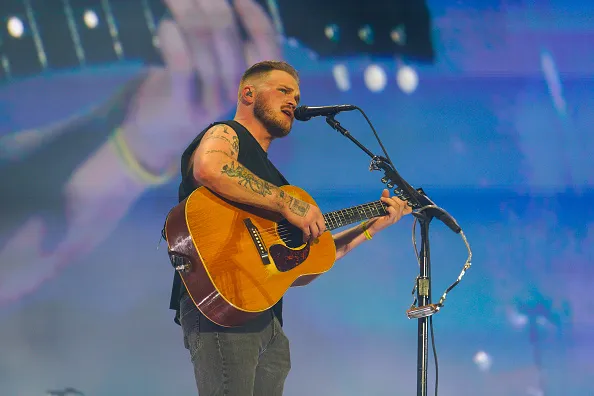 Zach Bryan performs during his concert, playing an acoustic guitar and singing into a microphone.