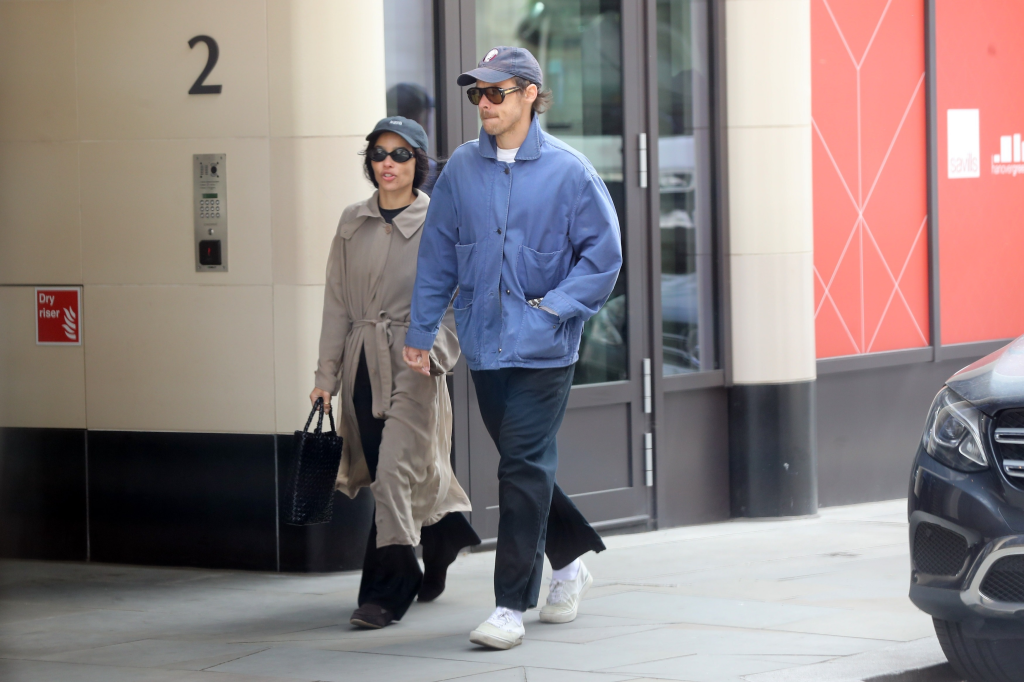 Zoe Kravitz in a trench coat and Harry Styles in a blue jacket walking outside.