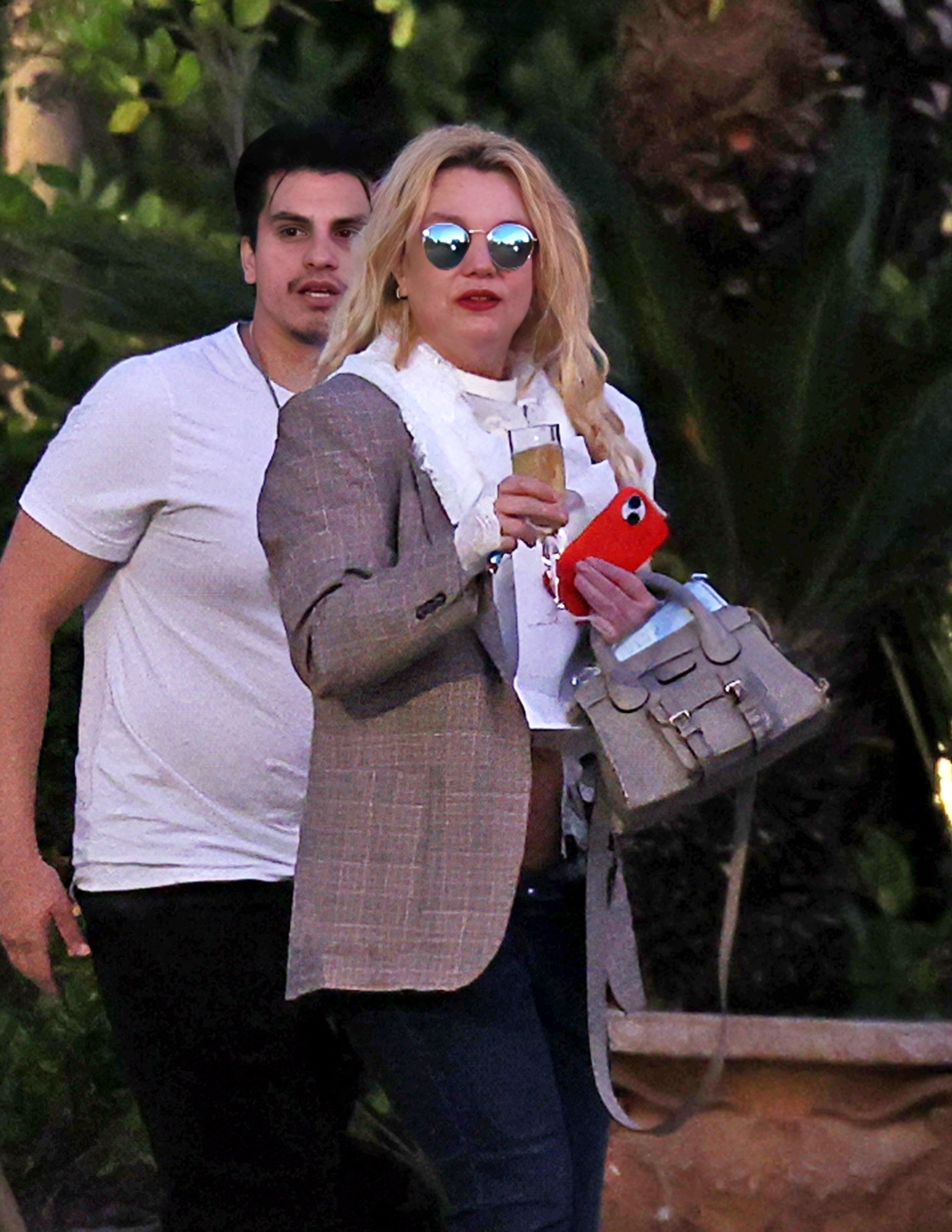 Britney Spears wearing sunglasses and holding a drink, next to a man in a white t-shirt.