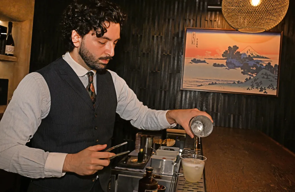 Bartender Damon Fabbo pours a cocktail into a glass.