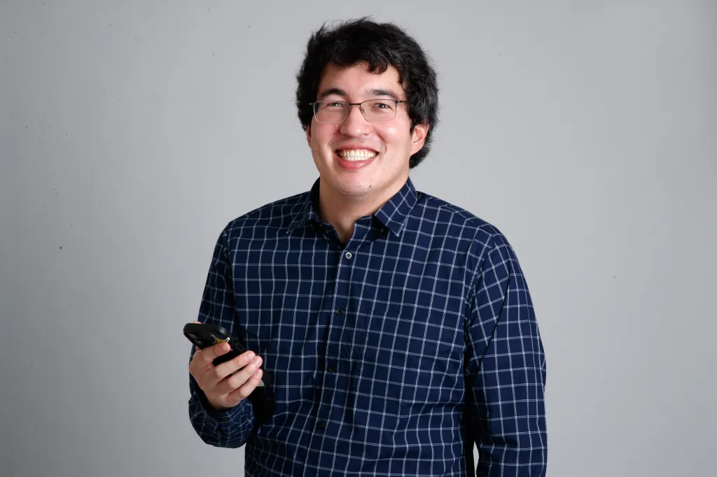 Benjamin Cost, a lifestyle reporter for the NY Post, smiles while holding a phone.