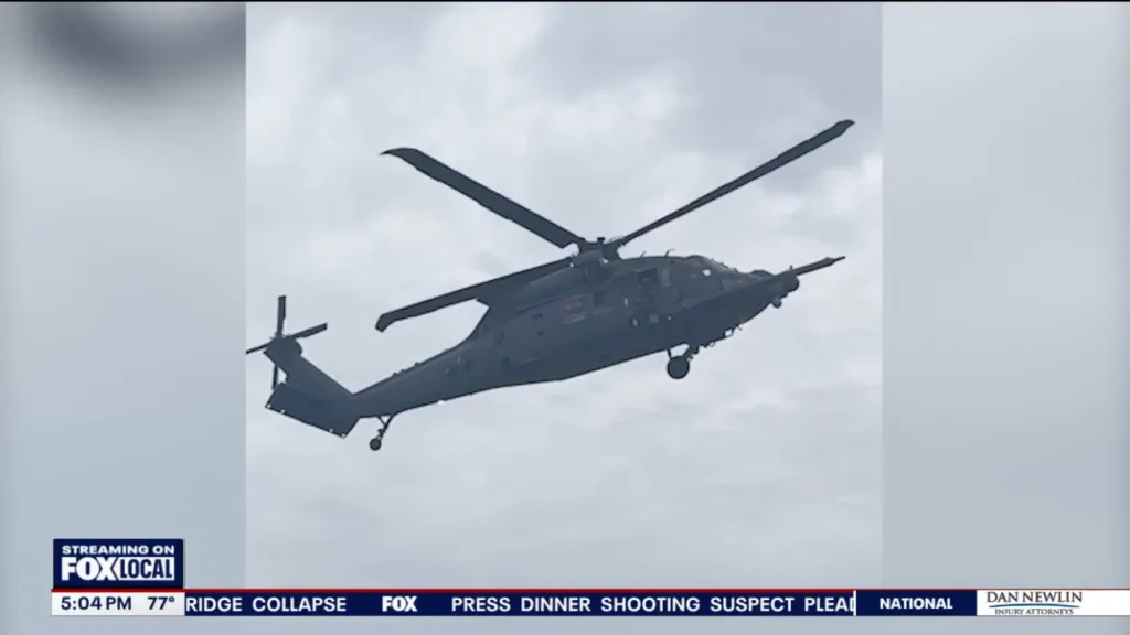 A dark gray helicopter flying against a cloudy sky.