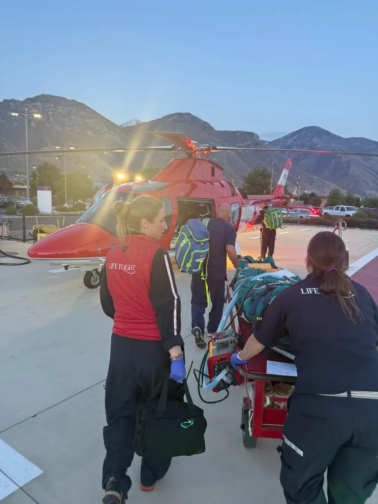 Medical personnel loading a patient on a stretcher into a red Life Flight helicopter.