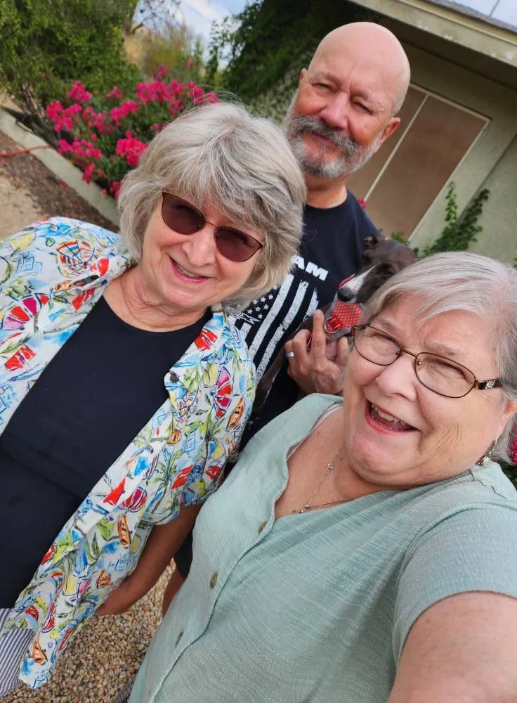 Two women smile at the camera, with a man and a small dog behind them.