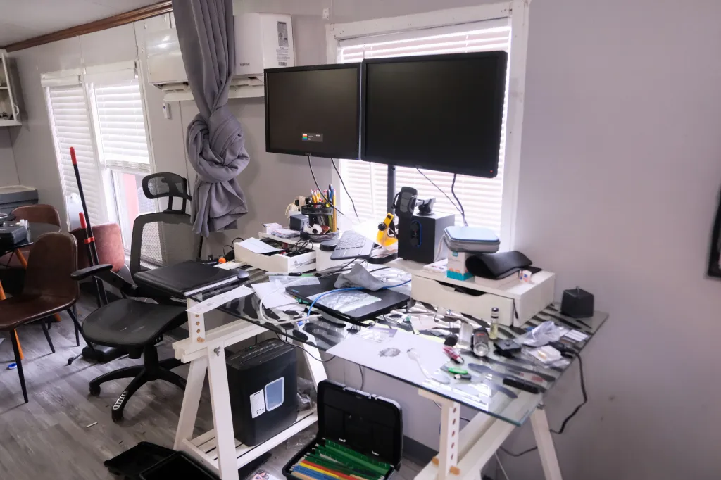 A cluttered office desk with two large monitors, a shredder, and various office supplies.