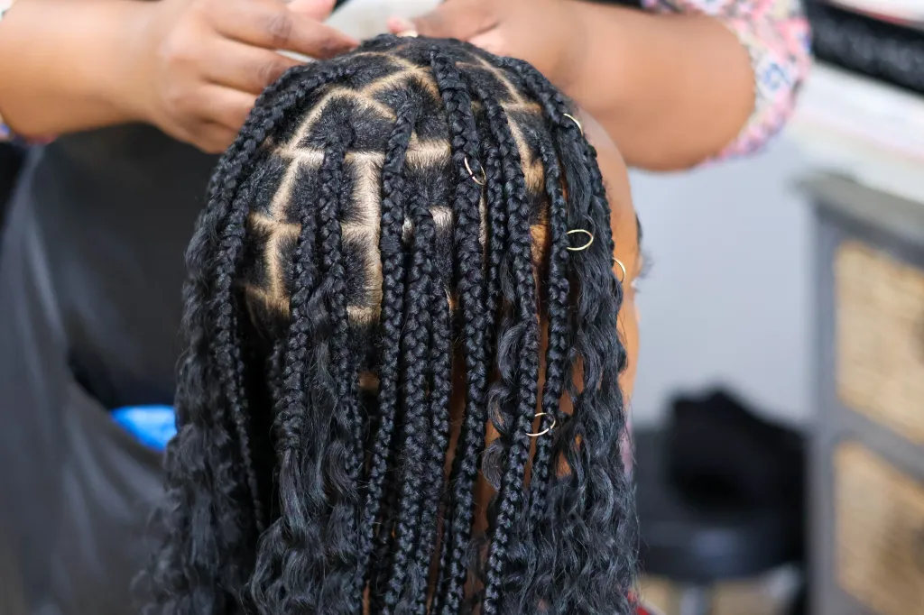 Close-up of a Black woman having her hair braided into box braids with gold rings.