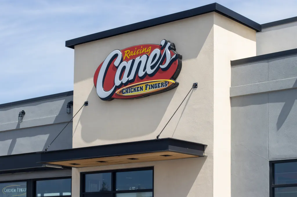 Exterior view of a Raising Cane's Chicken Fingers restaurant with its large red and white logo.