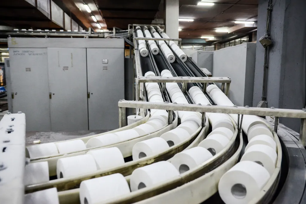 Toilet paper rolls moving along a production line conveyor belt in a factory.