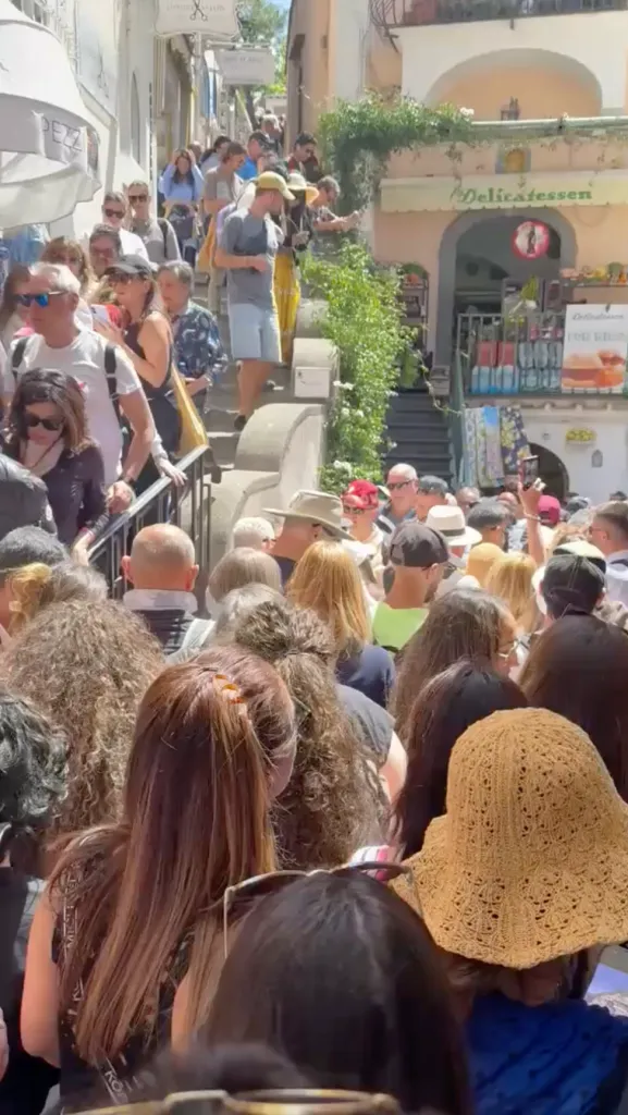 A crowded street with many people walking up and down stairs between buildings.