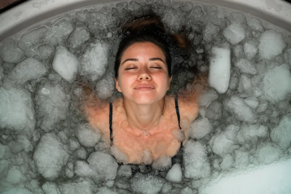 A woman with her eyes closed and a peaceful expression lies in an ice bath.