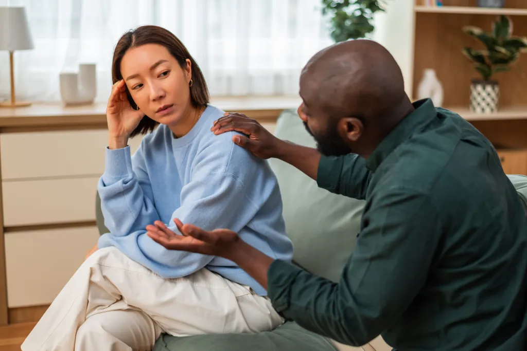 A Black man apologizing to an Asian woman, who looks upset and is turned away from him.
