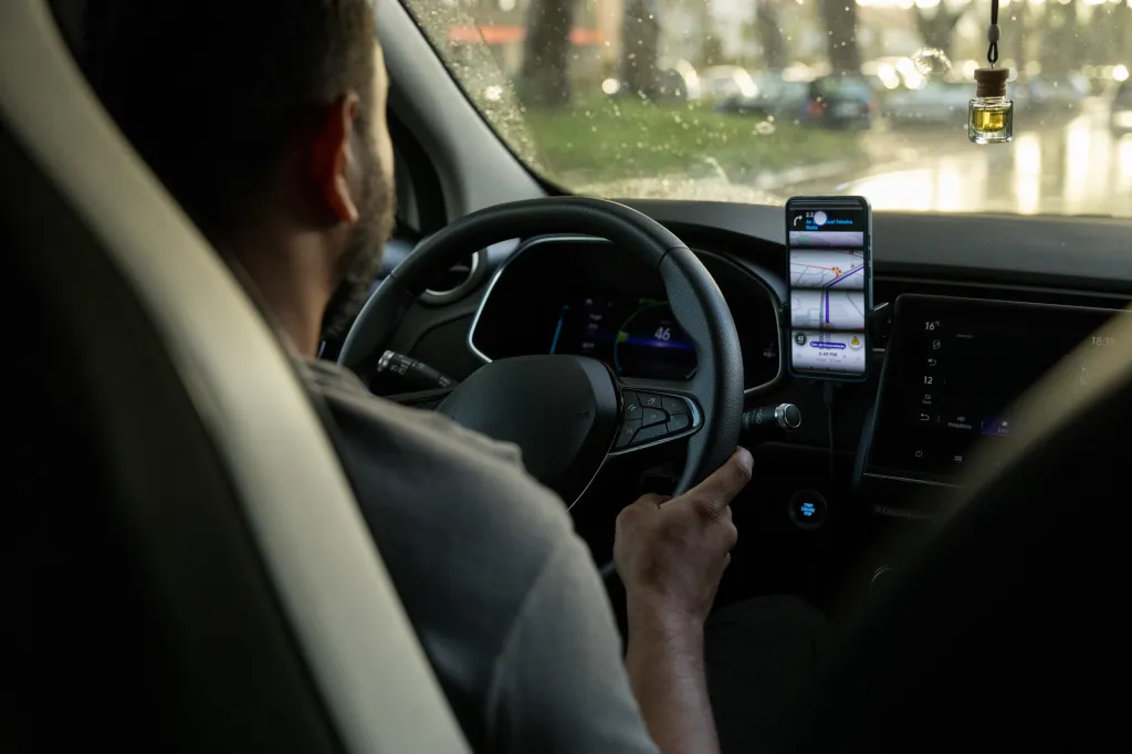person at the wheel of a car with a cell phone on the dashboard
