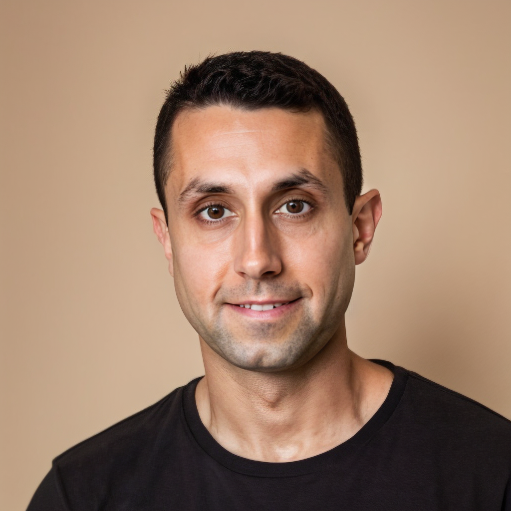 Headshot of a man with short dark hair, brown eyes, and a slight smile, wearing a black t-shirt against a light brown background.