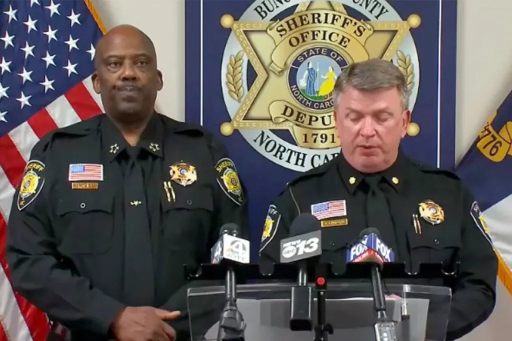 Two male police officers in uniform stand behind microphones with an American flag and the Buncombe County Sheriff's Office seal in the background.