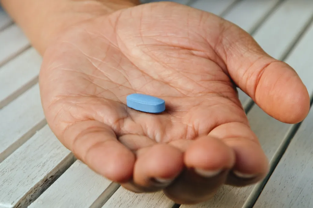 A person's open palm holds a single blue pill.