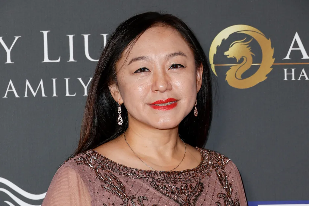 A woman with dark hair and a beaded dress smiles while wearing teardrop earrings and red lipstick.