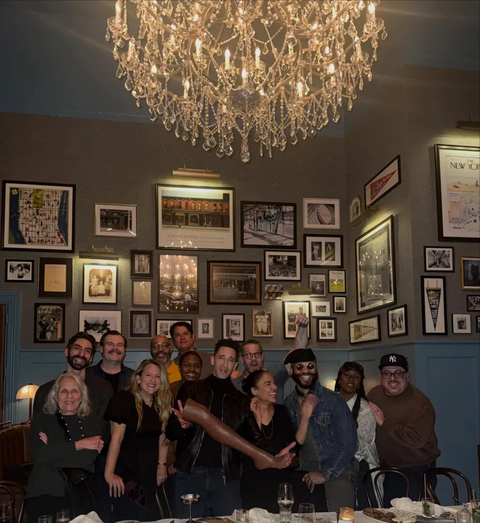 A group of people posing for a photo in a restaurant with many framed pictures on the wall and a large chandelier.