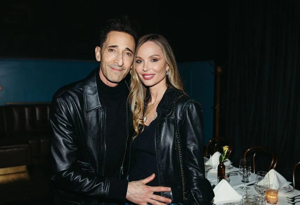 Adrien Brody and Georgina Chapman posing together in a dark room.