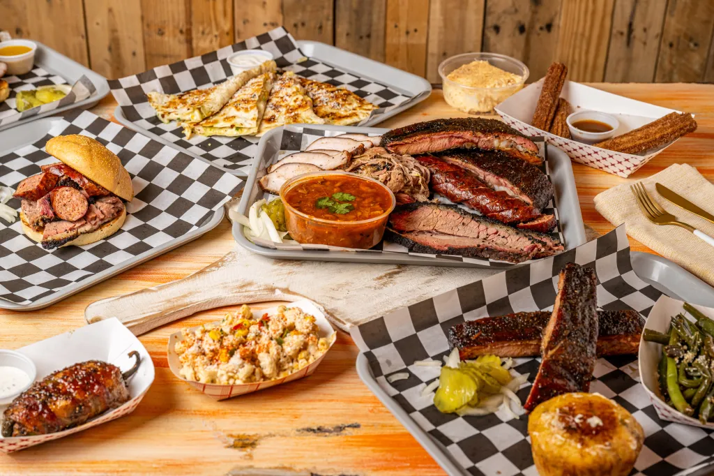 Collage of various barbecue dishes, including ribs, brisket, sausage, salad, quesadillas, and churros on trays and checkered paper.