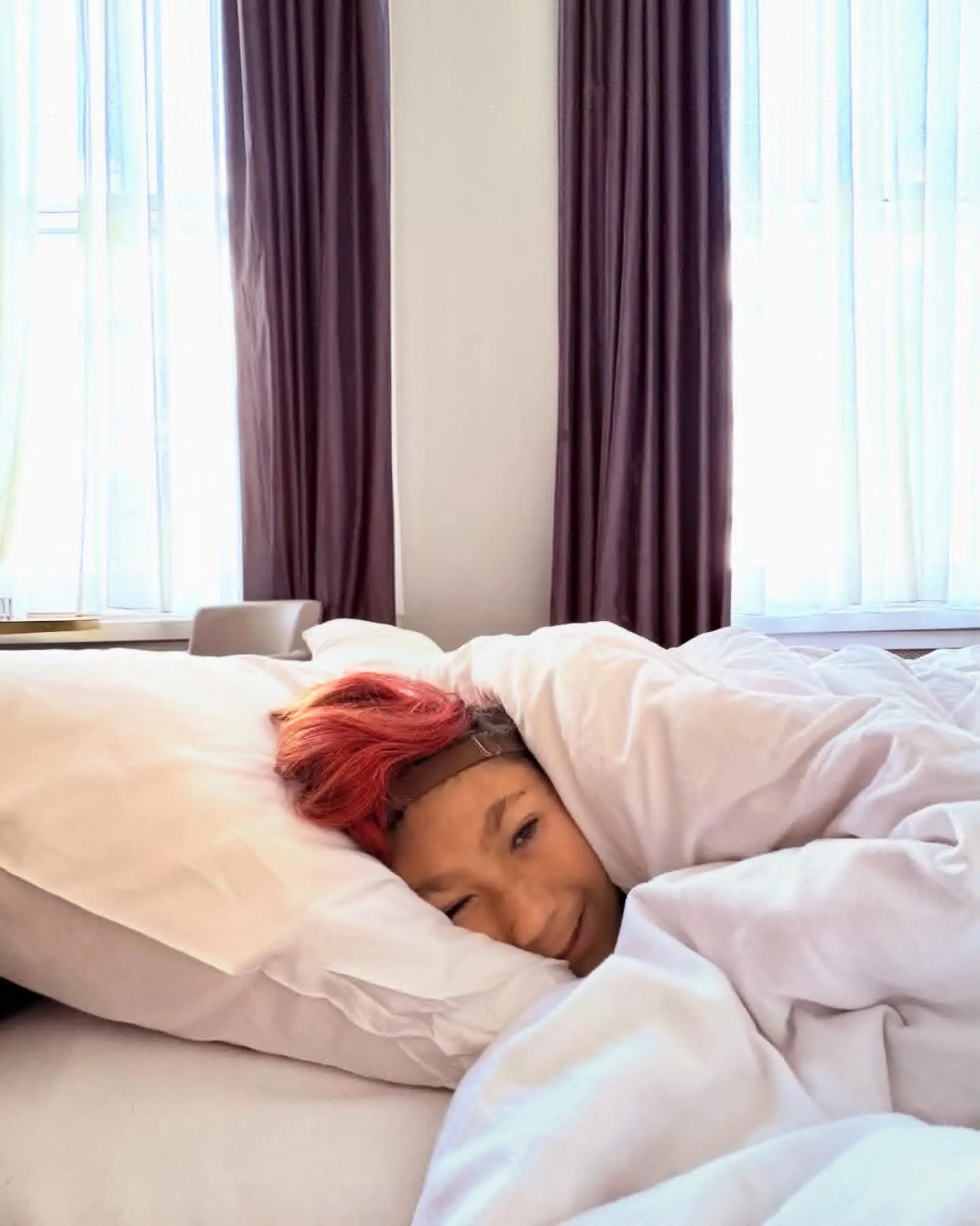 Isaac under a white duvet with red hair on a pillow.