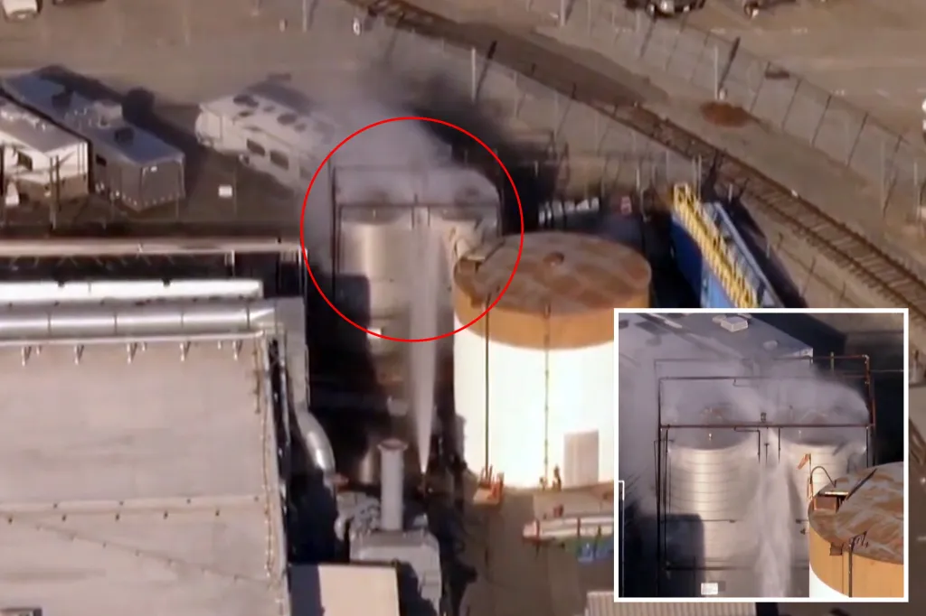 Aerial view of storage tanks releasing steam and being sprayed with water at a plant.