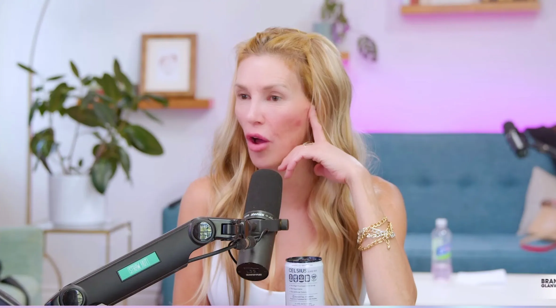 Brandi Glanville with an open mouth and hand near her face, next to a microphone and a 