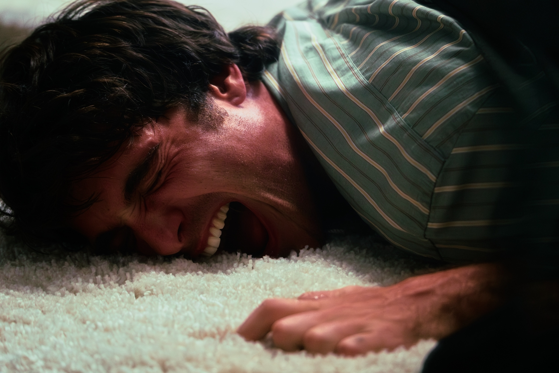 Man lying on a white shag carpet, screaming.
