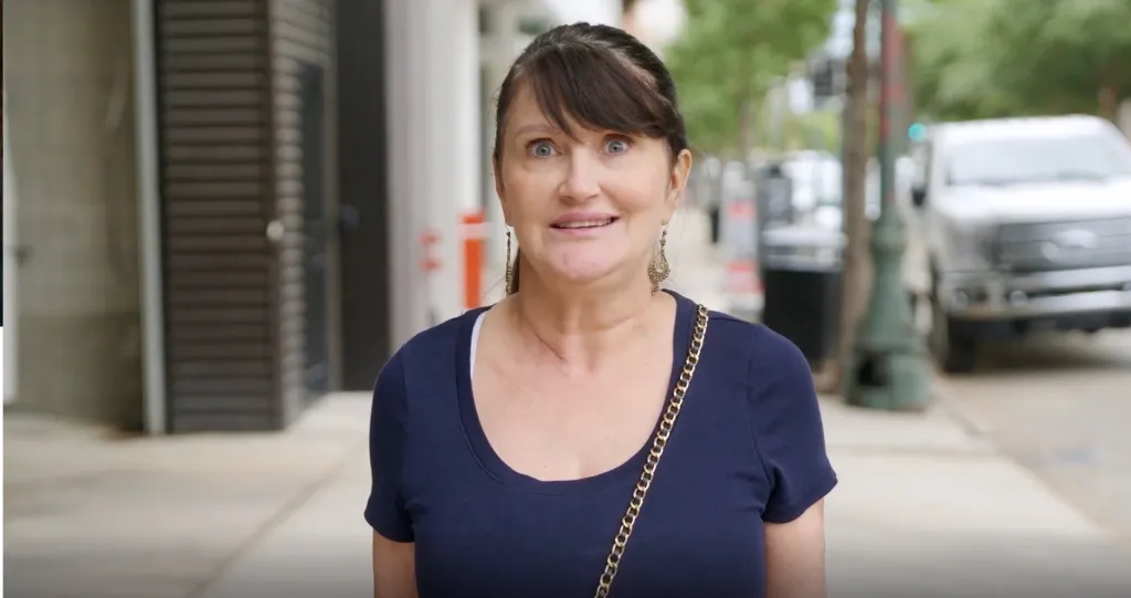 A woman in a blue shirt with a gold-chain purse smiles uncertainly.