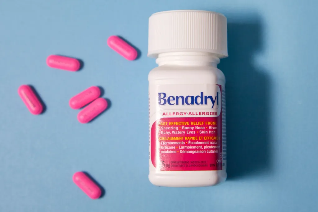 A bottle of Benadryl Allergy medication with several pink Benadryl capsules scattered on a blue background.