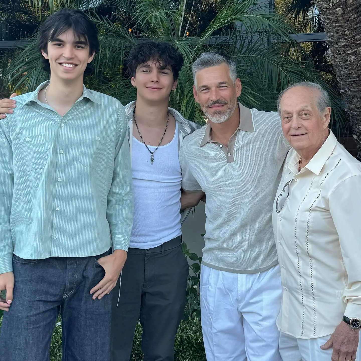 Four men smiling in front of palm trees.